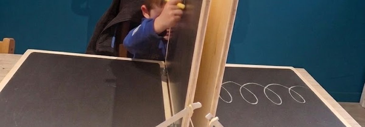 Un enfant trace des boucles sur le tableau de Mesker, un support à panneaux articulés pour travailler le geste d'écriture